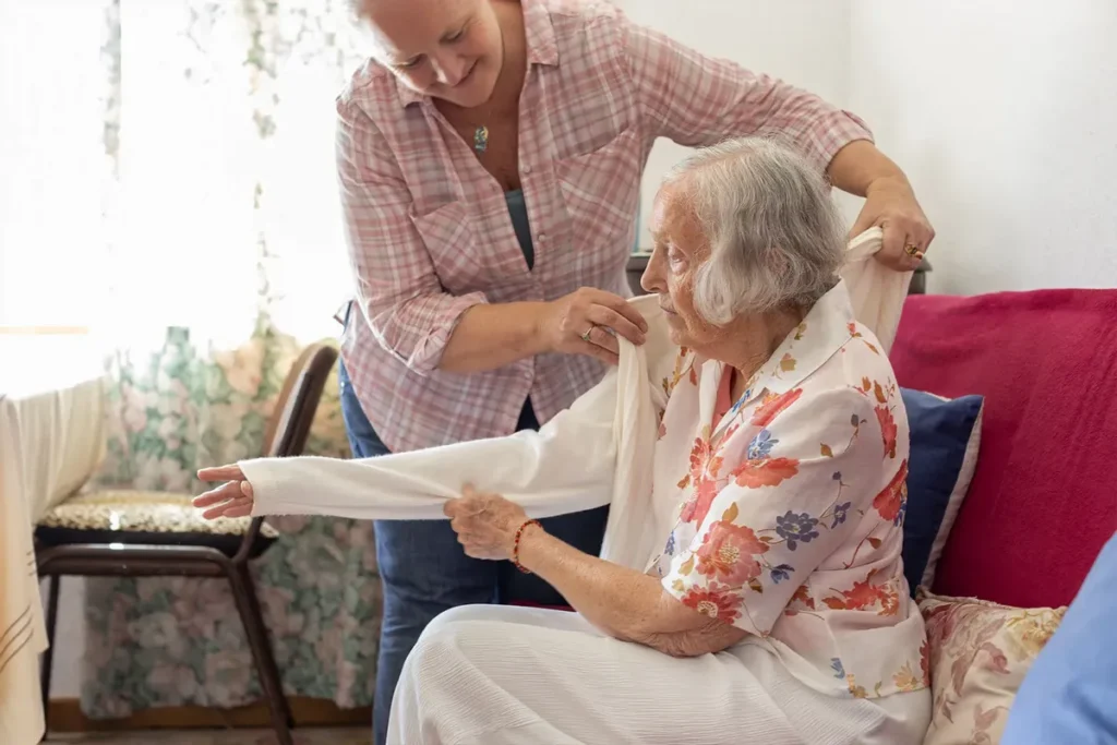 Caregiver helping elderly patient put a sweater on