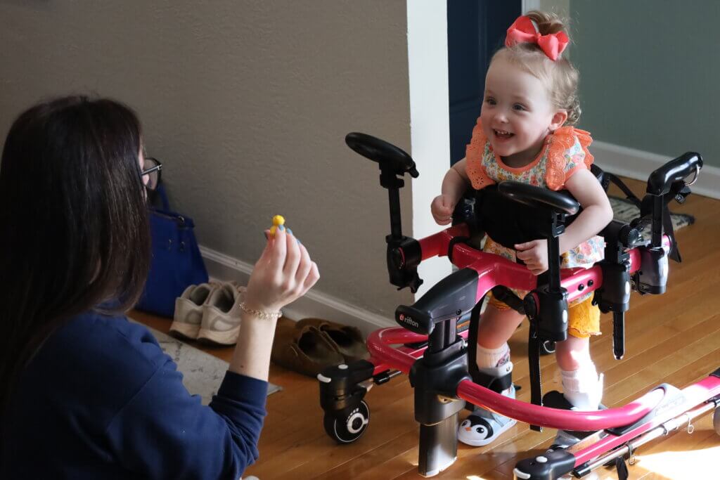 Quinn using equipment to walk toward her therapist Sam